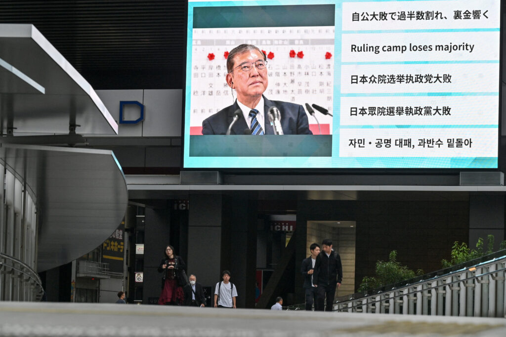People walk along an elevated walkway under a large television screen showing images of Japan's Prime Minister Shigeru Ishiba one day after the general election in Tokyo on October 28, 2024. (AFP)