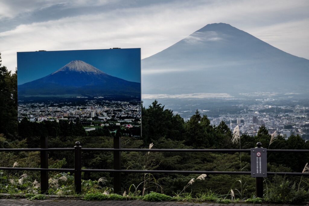 A sign with a photo of Mount Fuji covered in snow is seen at a view point as Mount Fuji, the highest mountain in Japan at 3,776 metres, looms in the background in Gotemba, Shizuoka prefecture on October 31, 2024. (AFP)