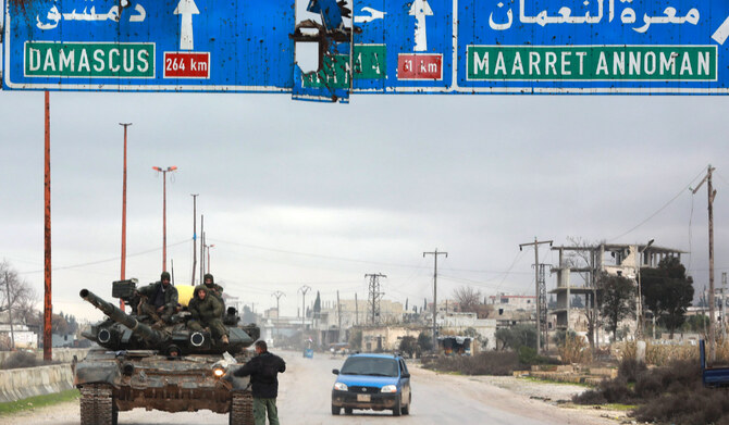 A Syrian army tank stationed under a road sign indicating the direction to the capital Damascus and the town of Maaret al-Numan, on a highway in the northwest of the country, on January 30, 2020. (AFP)