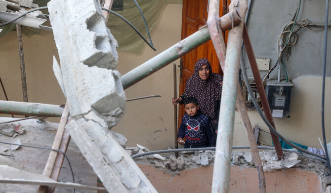 A Palestinian woman and a child stand at the door of a house next to a building destroyed during an Israeli strike in the Nuseirat camp in the central Gaza Strip, on December 10, 2024, amid the ongoing conflict in the Palestinian territory between Israel and Hamas. (AFP)