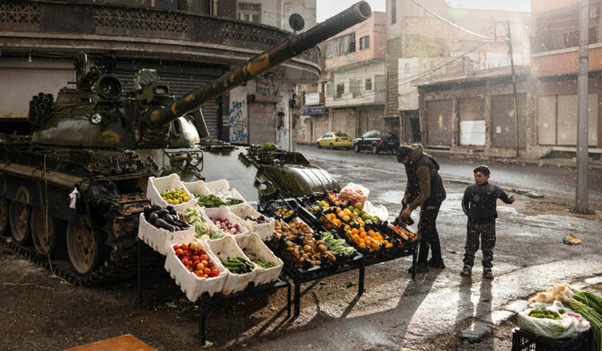 A Syrian man sells vegetables in front of a damaged tank in Homs, on December 20, 2024. (AFP)