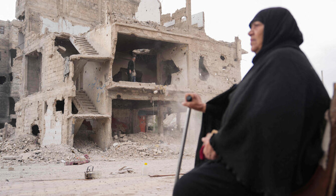 A woman sits on a chair on the street as a man clears rubble and debris from a damaged house at the Yarmuk camp for Palestinian refugees south of Damascus on December 22, 2024. (AFP)