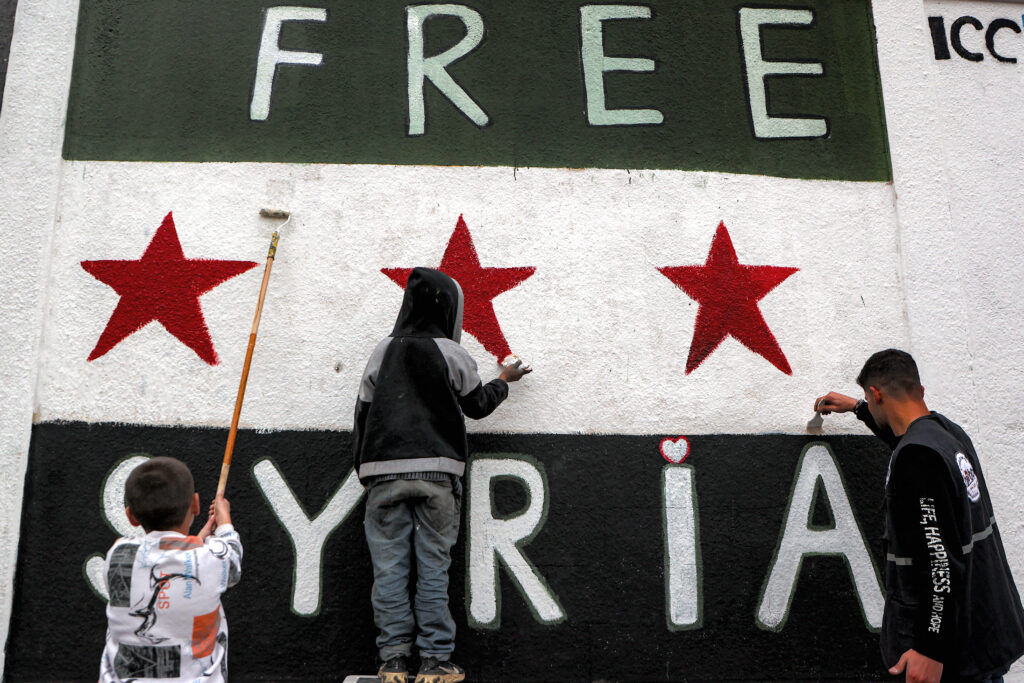 A man and children paint a mural depicting the independence-era Syrian flag with the slogan