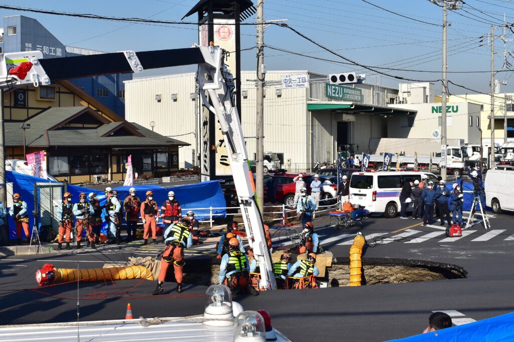 Firefighters work to rescue a truck driver after his vehicle was swallowed up by a sinkhole at a prefectural road intersection, in the city of Yashio, Saitama Prefecture on January 28, 2025. (Photo by JIJI Press / AFP)