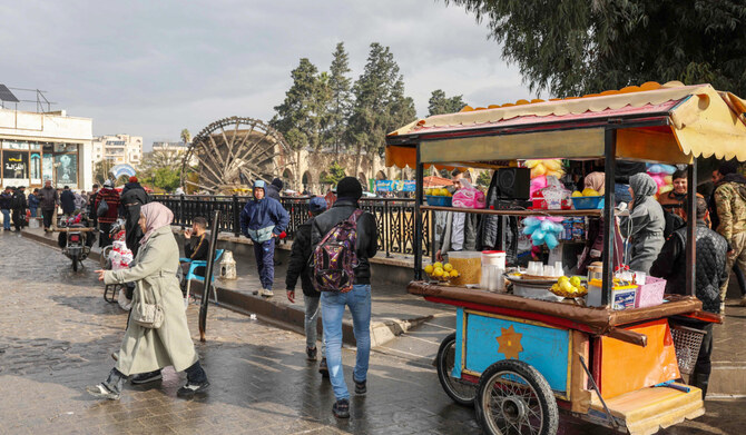People and street vendors move past one of Hama's landmark historic water wheels, or norias, on a bridge over the Orontos riverbank in the heart of the central Syrian city on December 30, 2024. (AFP)