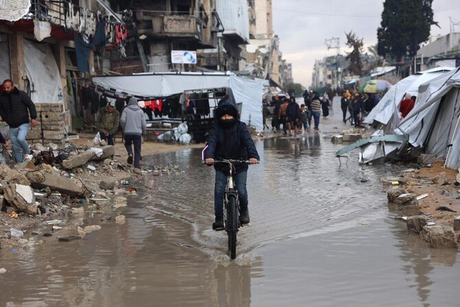 A displaced Palestinian rides his bicycle through a puddle of water near a makeshift camp during a storm in Gaza City on December 31, 2024. (AFP)