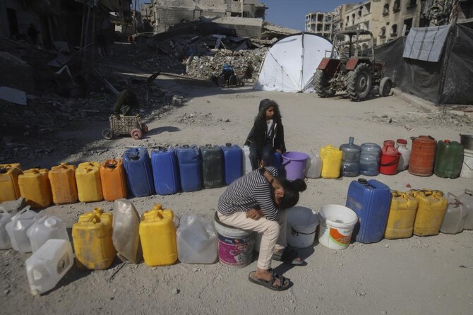 Palestinian children wait next to a row of jerrycans to collect water in Beit Lahia. (AP)