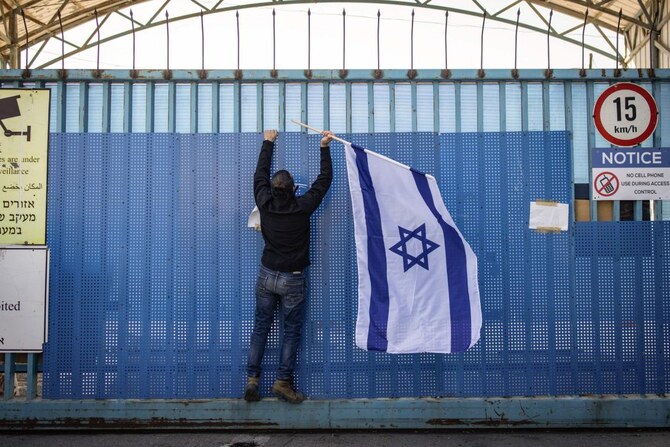 An Israeli right-wing activist hangs a national flag at the shuttered gate of UNRWA's West Bank Field Office in Jerusalem, Jan. 30 (AFP)
