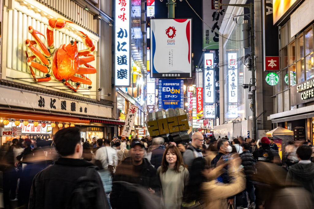 People walk along a street as the logo of Expo 2025 (top C) is seen in Osaka's Dotonbori district, one of the city's busiest tourist spots, on November 23, 2023. (AFP)