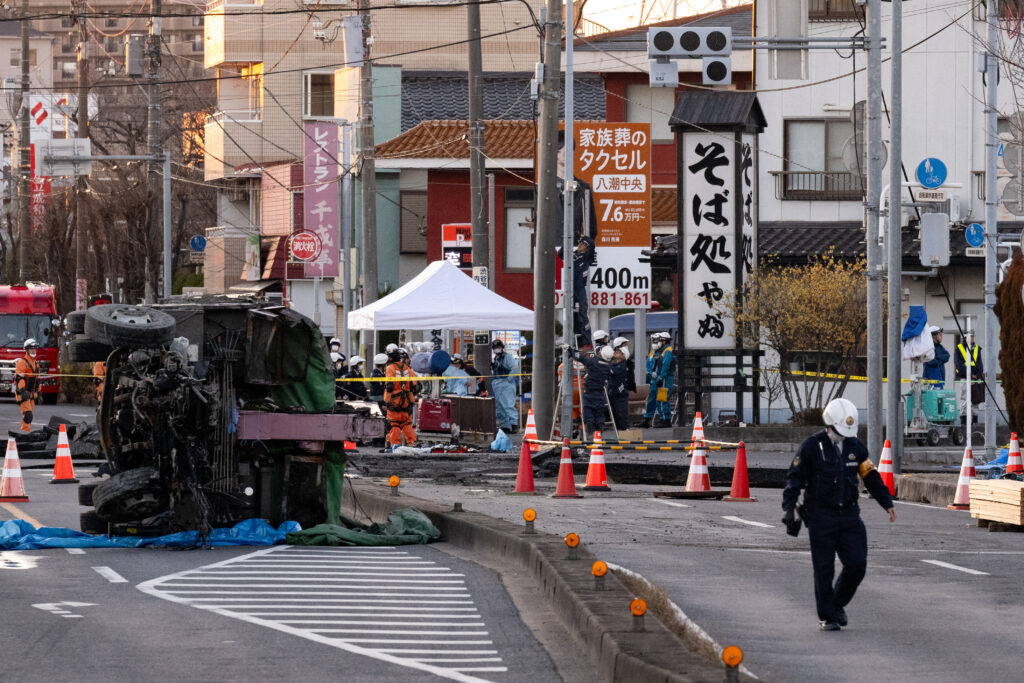 Part of a truck salvaged from a sinkhole sits on its side as rescue operations continue for the driver at a prefectural road intersection in Yashio, Saitama Prefecture on January 30. (AFP)