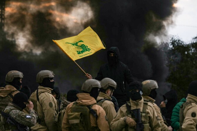 A Hezbollah supporter waves the group's flag in front of Lebanese army troops, as protesters burn tyres to block the road leading to Beirut’s international airport, Feb. 7. (AFP)