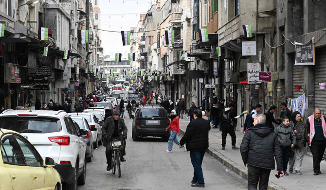 People walk past shops in Homs on February 10, 2025. (AFP)