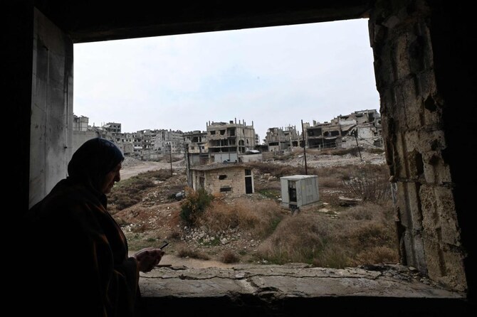 A displaced Syrian stands inside her dilapidated apartment, overlooking the destruction in Homs' Khaldiyeh neighborhood. (AFP)