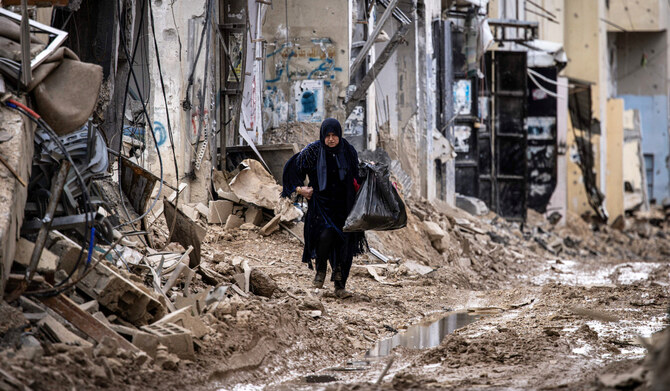 A displaced Palestinian woman carries her personal belongings as she walks past damaged buildings in the Jenin camp for refugees in the occupied West Bank on February 24, 2025. (AFP)