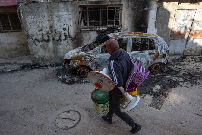 A man carries housewares as he walks past a burnt car while fleeing the Nur Shams camp for Palestinian refugees near Tulkarem (AFP)