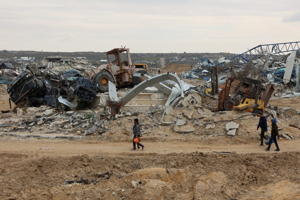 Displaced Palestinians walk past destroyed vehicles as they cross the Netzarim corridor as they make their way to the northern parts of the Gaza Strip on February 9, 2025. (AFP)