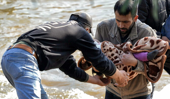 A man receives a blanketed child from another crossing the Nahr al-Kabir river, forming the border between Syria's western Latakia province and northern Lebanon in the Hekr al-Daher area on March 11, 2025. (AFP)