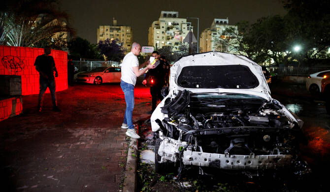People stand near a damaged car at an impact scene following a hit by a rocket fired from the Gaza strip towards Israel, in Ashkelon, Israel April 6, 2025. (REUTERS)