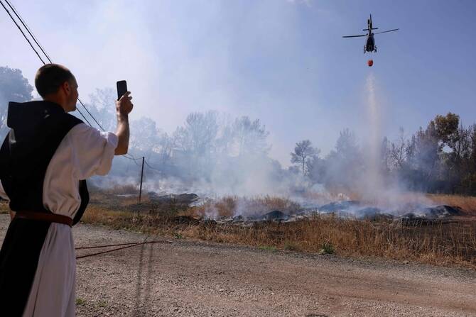 A monk watches as a firefighter helicopter drops flame retardant while trying to extinguish a forest fire near Latrun Monastery in central Israel, on May 1, 2025. (AFP)
