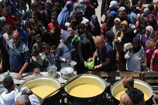 Palestinians queue for a portion of hot food distributed by a charity kitchen at the Nuseirat refugee camp in the central Gaza Strip on May 5, 2025. (AFP)