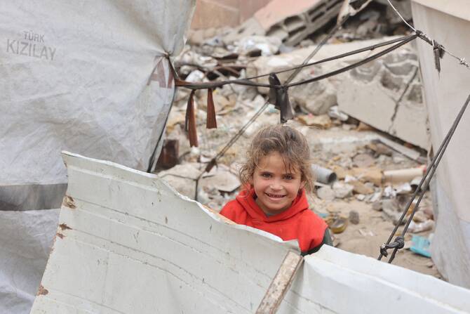 A Palestinian girl smiles while playing near her tent at a makeshift displacement camp set up amid building rubble in Gaza City, May 12, 2025. (AFP)
