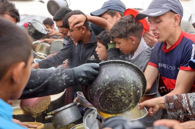 Palestinian youths shove to get a ration of hot food from a charity kitchen set up at the Islamic University campus in Gaza City on May 12, 2025. (AFP)