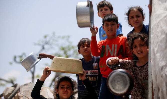 Palestinians wait to receive food cooked by a charity kitchen, in Jabalia, in the northern Gaza Strip, May 14, 2025. (Reuters)
