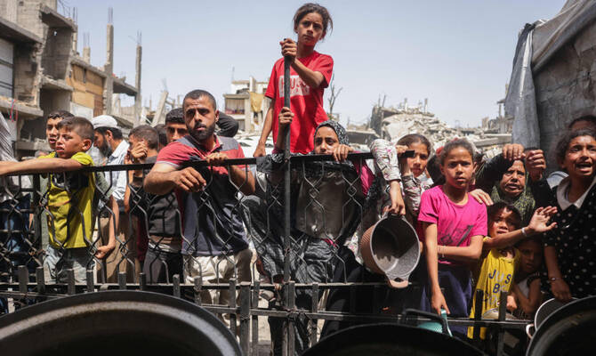 Palestinians wait to get a portion of cooked food from a charity kitchen in Jabalia in the northern Gaza Strip on May 17, 2025. (AFP)