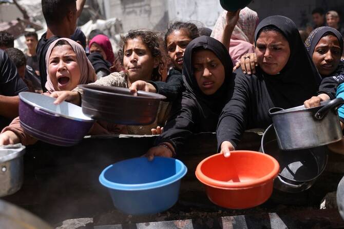 Displaced Palestinians gather to collect portions of cooked food at a charity distribution in Jabalia in the northern Gaza Strip on May 19, 2025. (AFP)