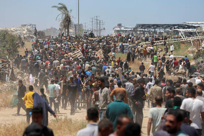 People walk as Palestinians receive aid supplies from the US-backed Gaza Humanitarian Foundation, in the central Gaza Strip, May 29, 2025. (REUTERS)