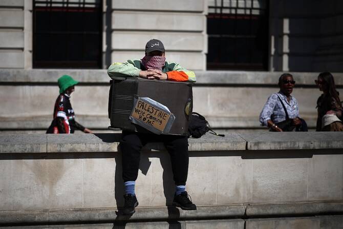 A person sits with a suitcase sign reading ‘Palestine: We’re Coming Home’ as they take part in a pro-Palestinian march through central London on May 17, 2025. (AFP)