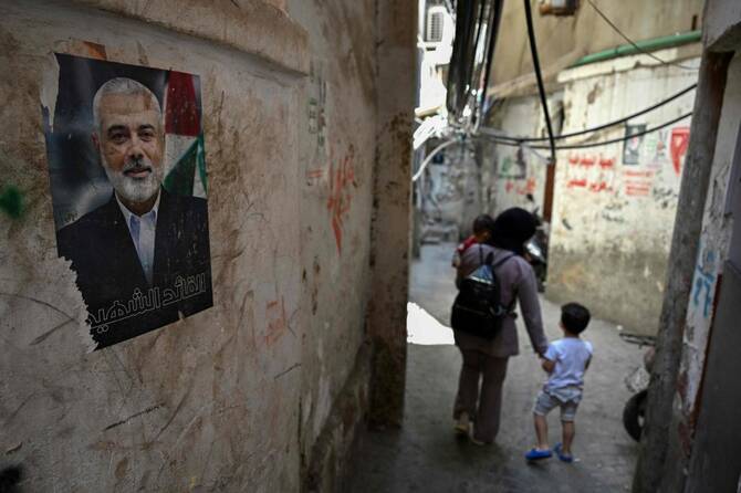People walk past a portrait of Palestinian Hamas movement’s slain political chief Ismail Haniyeh in a narrow alleyway at the Burj al Barajneh camp for Palestinian refugees in Beirut’s southern suburbs on May 20, 2025. (AFP)