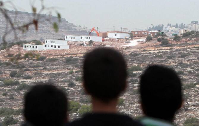 Palestinian children from the village of al-Mazraa al-Qabaliya look a bungalows in the distance built by Israeli settlers at an outpost constructed on seized land from the Palestinian village, near the West Bank city of Birzeit on December 3, 2013. (File/AFP)
