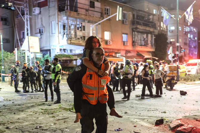 A rescuer carries an injured girl on his back in an area hit by a missile fired from Iran, in Ramat Gan near Tel Aviv on June 13, 2025. (AFP)