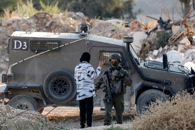 A woman speaks with an Israeli army soldier standing outside an armoured vehicle at a cemetery in Jenin in the occupied West Bank, June 6, 2025. (AFP)
