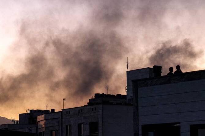 People stand on a rooftop amidst billowing smoke following an overinght Israeli strike in Tehran on June 17, 2025. ( AFP)