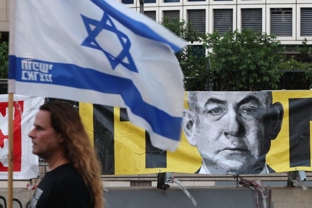 A demonstrator carrying the Israeli flag walks past a portrait of Prime Minister Benjamin Netanyahu during an anti-government protest in Tel Aviv on June 7, 2025. (AFP)