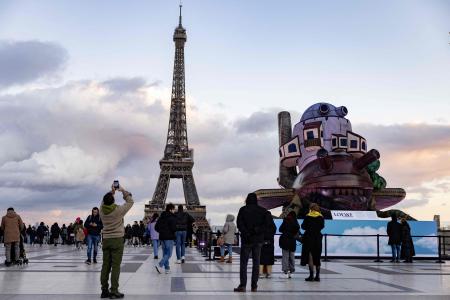 (FILES) This file photo taken on January 20, 2023 shows members of the public taking photographs in front of the Eiffel Tower and near an inflatable installation picturing Japanese director, animator and manga artist Hayao Miyazaki's movie 