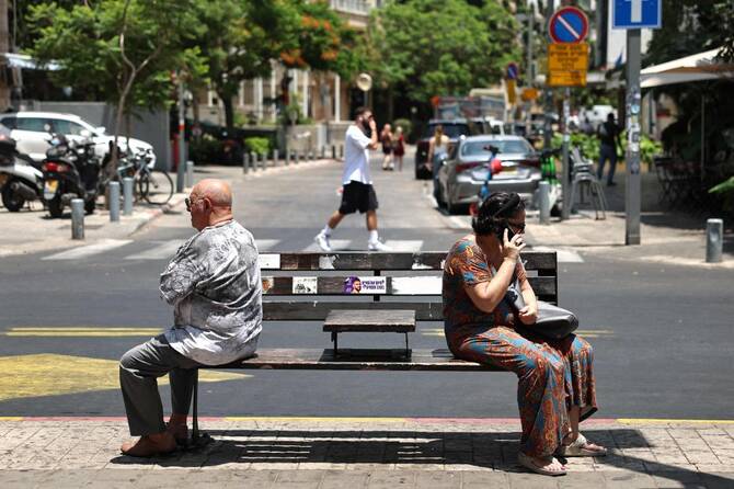 A woman sitting on a bench speaks on her mobile phone, as a man sits resting near her, the day after Israel and Iran exchanged missile fire, in Tel Aviv, June 25, 2025. (AFP)