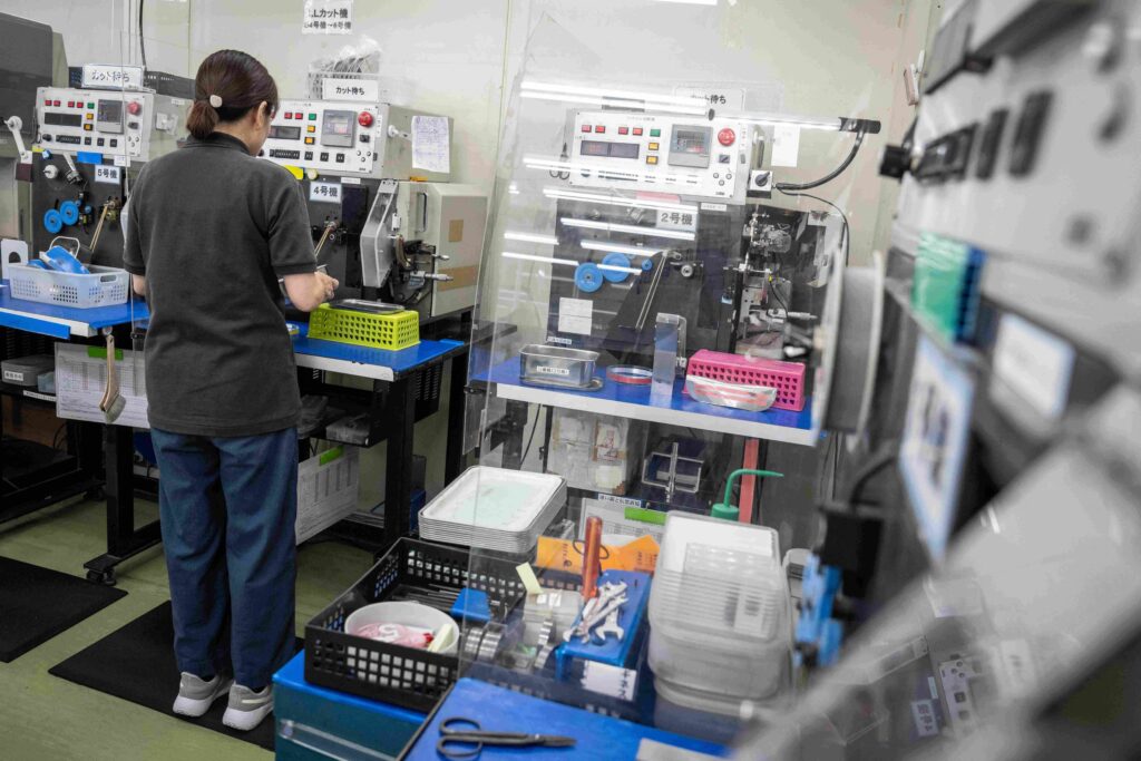 A member of staff works on a production line that manufactures small metal coils at Mitsuwa Electric in Tokyo on July 11, 2025. (AFP)