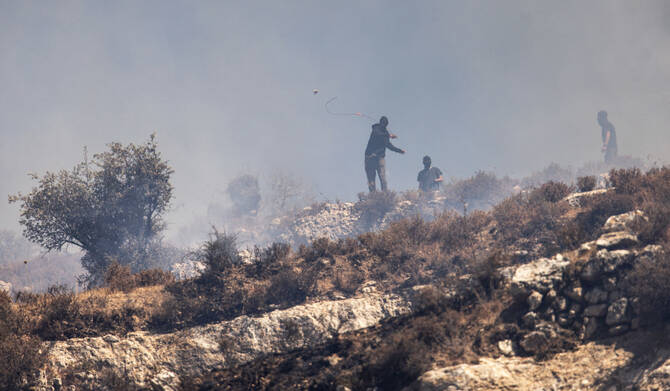 Masked Israeli settlers hurl rocks at Palestinians from hilltop in the village of Sinjil, in the occupied West Bank on July 4, 2025. (AFP)