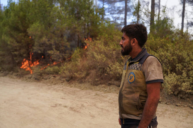 A Syrian Civil Defense worker, also known as the White Helmets, stands watching a wildfire, in Latakia countryside, Syria, July 6, 2025. (Reuters)