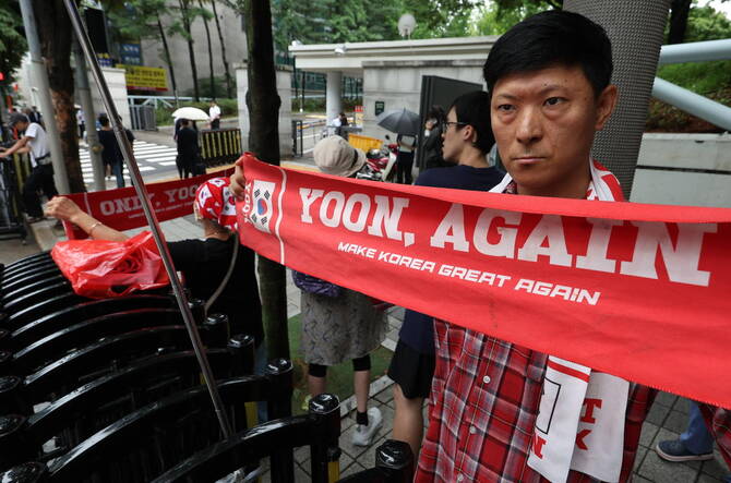 Above, a supporter of jailed former President Yoon Suk Yeol holds up a sign, which reads ‘Yoon, Again,’ in front of the Seoul Central District Court in Seoul on July 18, 2025. (EPA/Yonhap)