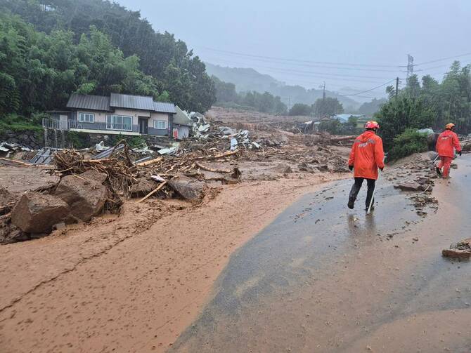 Rescue members stand on a mud-covered road after a landslide hit a village in southern Sancheong county as heavy rain continued to pound the country. (Gyeongsangnam-do Fire Department via AFP)