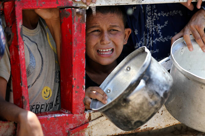 A child reacts as Palestinians gather to receive food from a charity kitchen, amid a hunger crisis, in Gaza City, July 22, 2025. (Reuters)