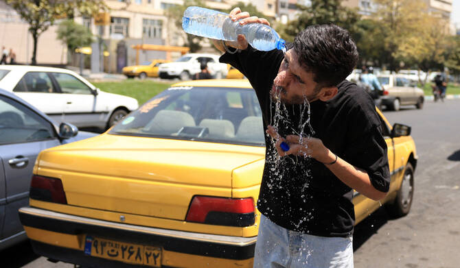 An Iranian taxi driver cools down by splashing water on his face on a street amid soaring temperatures in Tehran on July 22, 2025. (AFP)