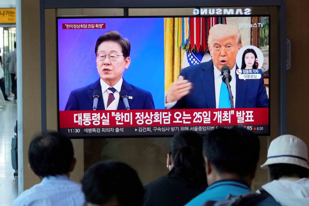 People watch a TV screen showing a file image of South Korean President Lee Jae Myung, left, and U.S. President Donald Trump during a news program at the Seoul Railway Station in Seoul, South Korea, Tuesday, Aug. 12, 2025. The signs read,