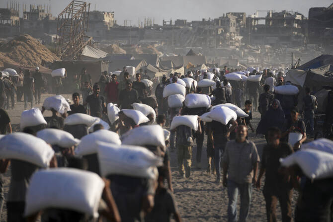 Palestinians carry sacks of flour unloaded from a humanitarian aid convoy en route to Gaza City from the northern Gaza Strip on July 31, 2025. (AP Photo)