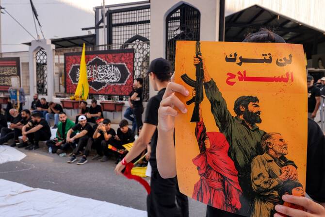 A person holds a sign with the Arabic slogan “we will not relinquish arms” as Lebanese Shiite Hezbollah supporters take part in a ceremony during the peak of Ashura in Beirut's southern suburbs, July 6, 2025. (AFP)