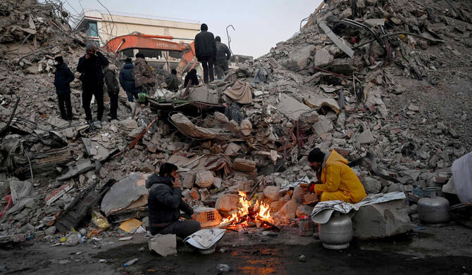 Relatives warm up around a fire in front of rubble of collapsed buildings as rescue teams continue to search victims and survivors, after a 7.8 magnitude earthquake struck the border region of Turkey and Syria earlier in the week, in Kahramanmaras on February 12, 2023. (AFP)